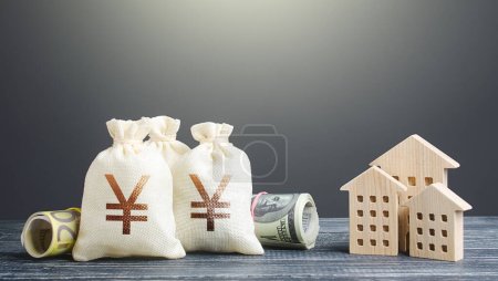 Photo for Yen Yuan money bags and residential buildings figures. Investments in real estate. Financing the construction and renovation of housing. Municipal budget management. Subsidies. Taxes. Mortgage loan - Royalty Free Image
