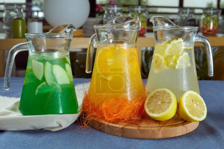Photo for Three varieties of summer lemonade in jugs on a blue tablecloth closeup - Royalty Free Image