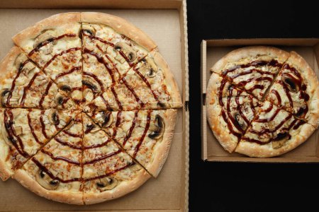 Photo for Large and small pizzas lie on an open cardboard box. Black background top view - Royalty Free Image