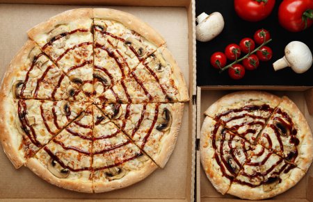 Photo for Large and small pizzas lie on an open cardboard box. Next to them are cherry tomatoes and mushroom mushrooms. top view - Royalty Free Image