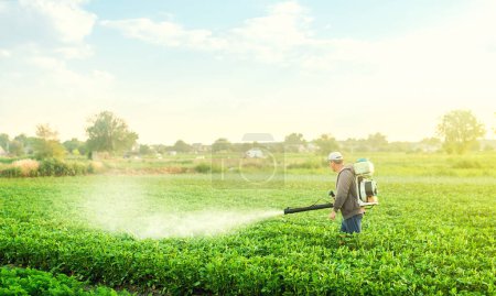 Photo for A farmer with a mist blower sprayer walks through the potato plantation. Use chemicals in agriculture. Agriculture and agribusiness. Treatment of the farm field against insect pests, fungal infections - Royalty Free Image
