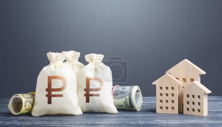 Photo for Russian ruble money bags and residential buildings figures. Investments in real estate. Municipal budget management. Taxes. Mortgage loan. Financing the construction and renovation of housing. - Royalty Free Image