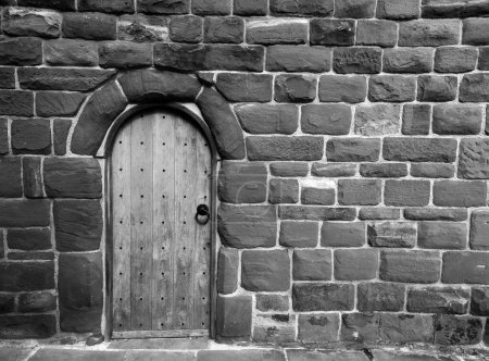 Foto de Imagen monocromática de una antigua puerta de madera en una pared medieval de piedra - Imagen libre de derechos