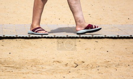 Téléchargez les photos : Les pieds des femmes en ardoises d'été sur la piste de sable de la plage - en image libre de droit