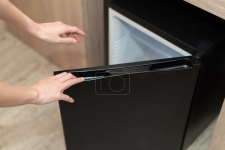 Téléchargez les photos : Femme main ouvrant la porte du réfrigérateur sur le sol en bois. - en image libre de droit