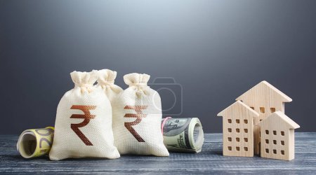 Photo for Indian rupee money bags and residential buildings figures. Investments in real estate. Mortgage loan. Financing the construction and renovation of housing. Municipal budget management. Taxes. - Royalty Free Image