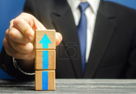 Photo for "Businessman builds a tower of blocks with an up arrow. Career promotion , growth of professional skills. Business development, expansion improvement. Profit growth. Marketing. Improving efficiency" - Royalty Free Image