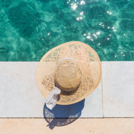 Photo for Woman wearing big summer sun hat relaxing on pier by clear turquoise sea. - Royalty Free Image