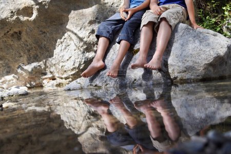 Foto de Dos niños (7-9 10-12) sentados en la roca por la sección baja del río - Imagen libre de derechos
