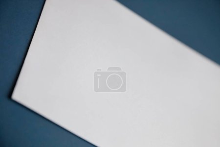 Téléchargez les photos : Image recadrée d'un papier blanc vierge sur une surface bleu foncé - en image libre de droit