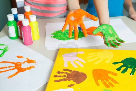 Photo for Close-up of paint covered hands and colorful handprints on papers - Royalty Free Image
