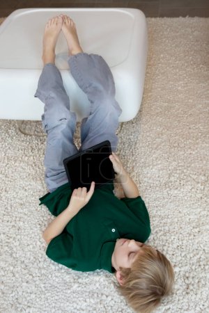 Téléchargez les photos : Jeune garçon couché sur un tapis avec tablette pc - en image libre de droit