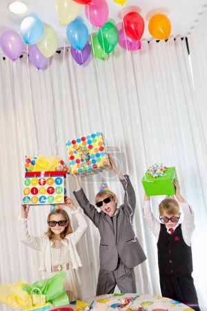 Photo for Brothers and sister wearing sunglasses holding gift aloft while shouting - Royalty Free Image