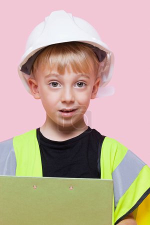Téléchargez les photos : Portrait d'un jeune garçon faisant semblant chez un ouvrier de la construction sur fond rose - en image libre de droit