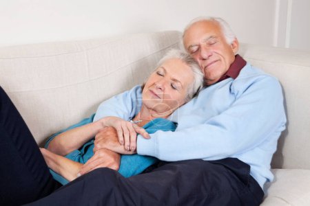 Photo for "Romantic senior couple with arms around relaxing on sofa at home" - Royalty Free Image