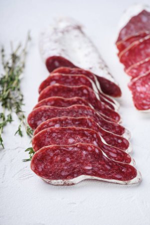Photo for Variety of dry cured fuet and salami sausages, whole and sliced on white textured background - Royalty Free Image