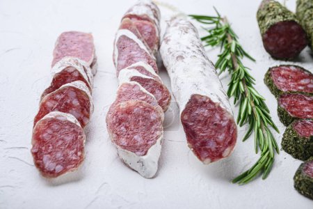 Photo for Variety of dry cured fuet and salami sausages, whole and sliced on white textured background - Royalty Free Image