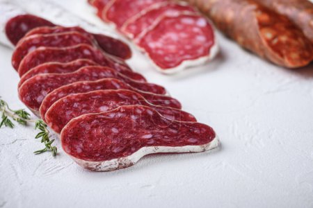 Photo for Variety of dry cured fuet and chorizosalami sausages, whole and sliced on white surface - Royalty Free Image