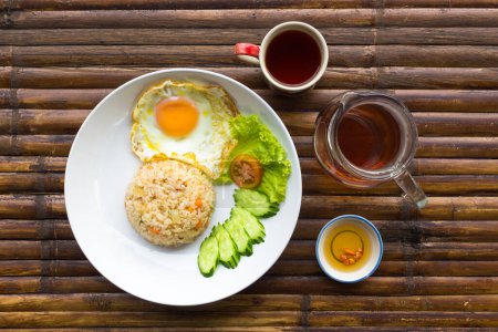 Foto de Huevo revuelto, arroz, verduras frescas en plato blanco, salsa, jarra y taza con té en mesa de bambú marrón. Tailandia desayuno. Vista superior. - Imagen libre de derechos
