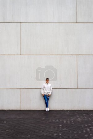 Téléchargez les photos : Portrait de jeune homme avec les mains sur la poche appuyé sur le mur à l'extérieur - en image libre de droit