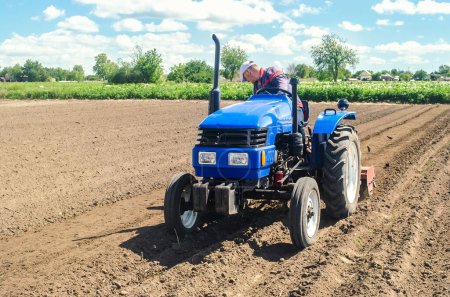 Photo for Farmer on a tractor loosens the soil with milling equipment. Loosening surface, land cultivation. Farming, agriculture. Plowing field. Use of agricultural machinery and to simplify and speed up work - Royalty Free Image