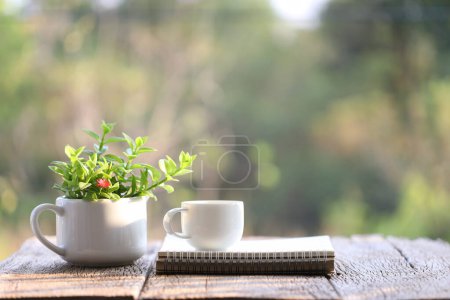 Photo for Spiral notebook and white coffee cup with plant in small cup pot on wooden table - Royalty Free Image