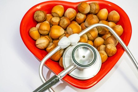 Photo for Shelled hazelnut heart figured on red plate and stethoscope for human health - Royalty Free Image