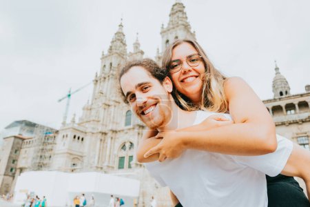 Téléchargez les photos : Young couple smiling to camera with the woman over the man in front of a touristic place - en image libre de droit