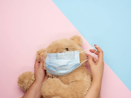 Foto de Gran osito de peluche en máscara médica sobre un fondo rosa azul - Imagen libre de derechos