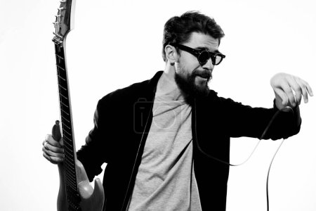 Téléchargez les photos : Un homme tient une guitare dans ses mains veste en cuir noir lunettes sombres performance musique fond clair - en image libre de droit