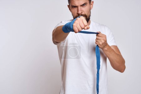 Foto de Un hombre deportivo con una camiseta blanca vendajes de boxeo en sus manos la práctica de ejercicios de golpe mejorar las habilidades - Imagen libre de derechos