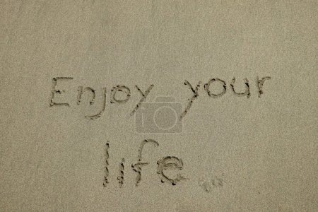 Foto de Disfrute de su vida, concepto de felicidad, pensamiento positivo, cita inspiradora escrita en la playa de arena - Imagen libre de derechos