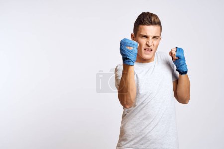 Téléchargez les photos : Boxeur masculin sportif en gants bleus pratiquant des coups de poing sur un fond clair - en image libre de droit