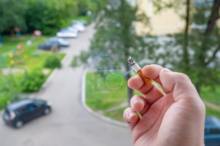 Téléchargez les photos : Main d'un fumeur qui tient une cigarette fumeur dans la fenêtre - en image libre de droit