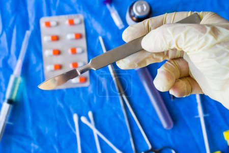 Photo for Hand with glove holding surgery blade, drugs, ampule, needle and blood tube - Royalty Free Image