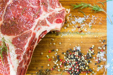Photo for "Raw beef meat on the table, spices and Rosemary, Rib eye steak ingredients. Pepper and coars salt." - Royalty Free Image