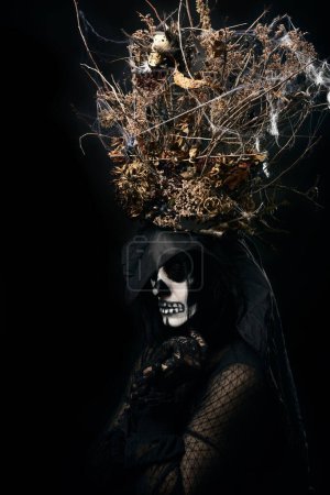 Téléchargez les photos : Femme en vêtements noirs et maquillage du crâne, une couronne de branches sèches - en image libre de droit