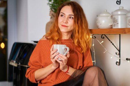 Téléchargez les photos : Une jolie fille aux cheveux roux s'assoit sur le tissu de toiture dans une cuisine élégante et confortable décorée pour Noël - en image libre de droit