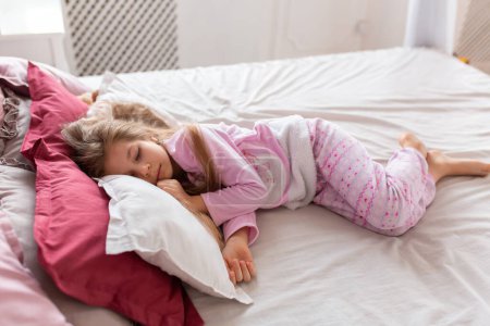Foto de Una niña en pijama rosa se duerme rápidamente en una cama cómoda - Imagen libre de derechos
