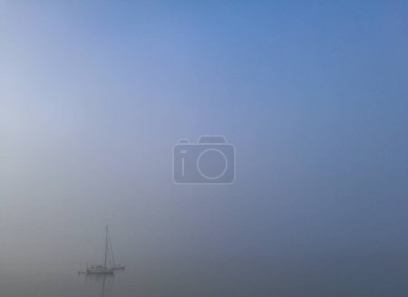 Téléchargez les photos : Océan froid et brumeux avec petit yacht blanc flottant sur la mer - en image libre de droit