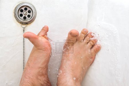 Téléchargez les photos : Se laver les pieds dans l'eau courante tout en étant couché dans une salle de bain close-up - en image libre de droit