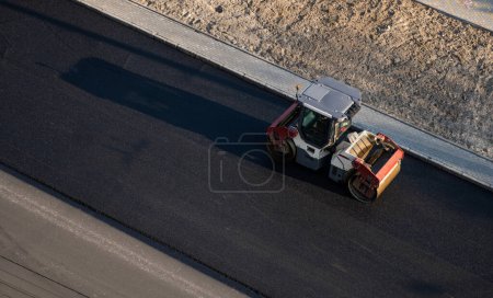 Foto de Rodillo de carretera de asfalto con compactador de rodillos de vibración pesada prensa nuevo asfalto caliente en la carretera en un sitio de construcción de carreteras. Rodillo de vibración pesada en el pavimento de asfalto de trabajo. Reparación - Imagen libre de derechos