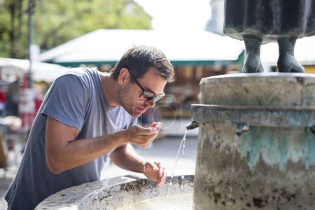 Foto de "Sediento joven cucasiano casual hombre beber agua de la fuente de la ciudad pública en un día caluroso de verano" - Imagen libre de derechos