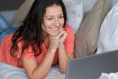 Téléchargez les photos : "La fille allongée sur le canapé se réjouit en regardant l'ordinateur portable. Sourires, " - en image libre de droit