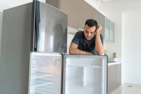 Foto de El tipo está triste cerca del refrigerador vacío sin comida. Servicio de entrega de alimentos publicidad - Imagen libre de derechos