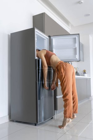 Foto de En un día caluroso, la chica se enfría con la cabeza en el refrigerador. Acondicionador de aire roto - Imagen libre de derechos