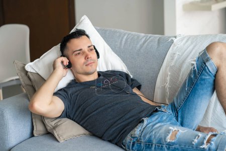 Photo for The guy enjoys the music while lying on the couch with headphones. Relaxation with music - Royalty Free Image