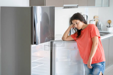 Téléchargez les photos : La fille est surprise par le réfrigérateur vide. Manque de nourriture. Livraison de nourriture - en image libre de droit