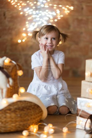 Foto de Adorable niña sentada en el suelo entre las guirnaldas de año nuevo - Imagen libre de derechos
