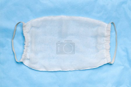 Photo for Handmade protective surgical face mask made from white sterile cheesecloth on blue medical background - Royalty Free Image